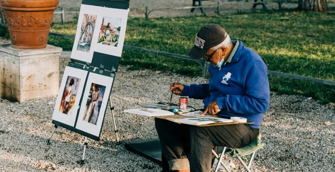 Street artist painting in a Roman park, showcasing artwork depicting famous landmarks.