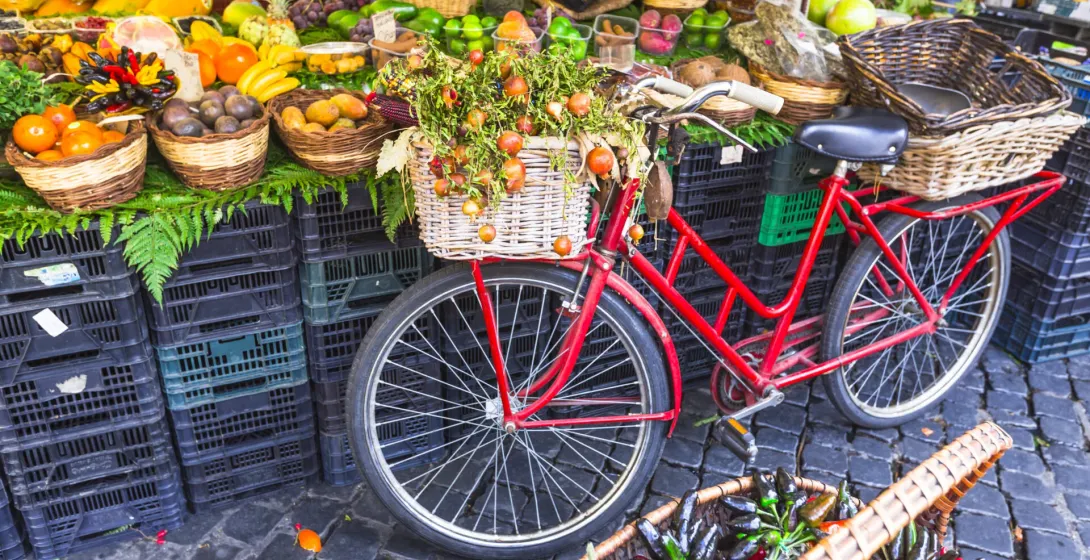 Red bicycle with fruit in basket at a vibrant Roman market.