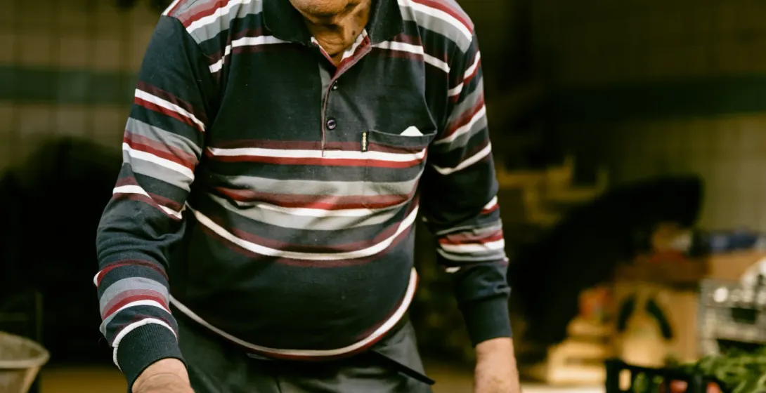An elderly vendor smiles while arranging cherries and plums at a Roman market.