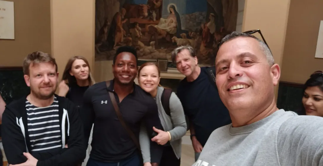 Happy tourists on a guided tour in Rome, posing for a selfie in front of a Nativity painting.
