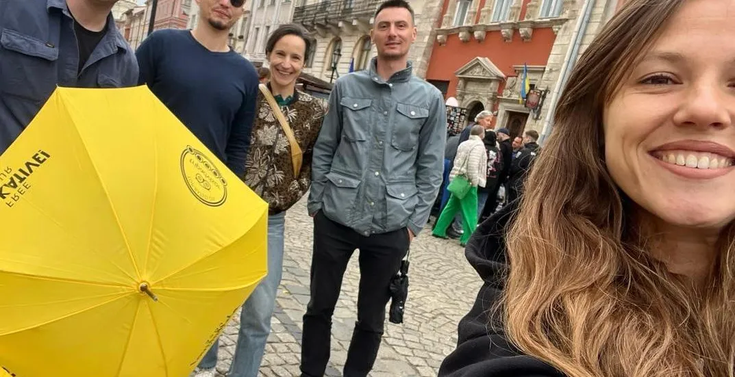 Group of five people, including a guide with a yellow Walkative umbrella, on a cobblestone street in Lviv's Old Town.