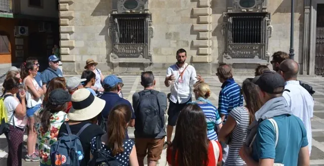 A tour guide leads a group of tourists through a historical square in Seville, Spain.