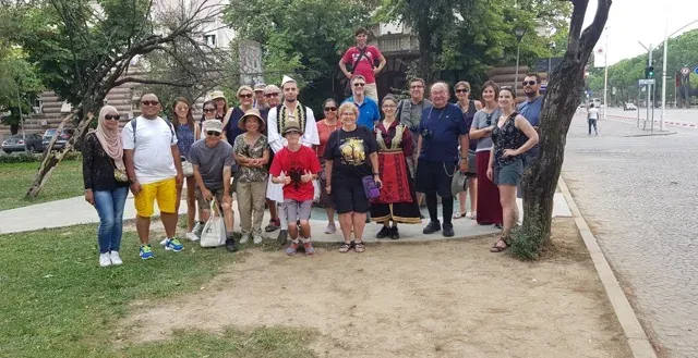 A diverse tour group smiles for a photo in Sofia, Bulgaria, near a historical monument.