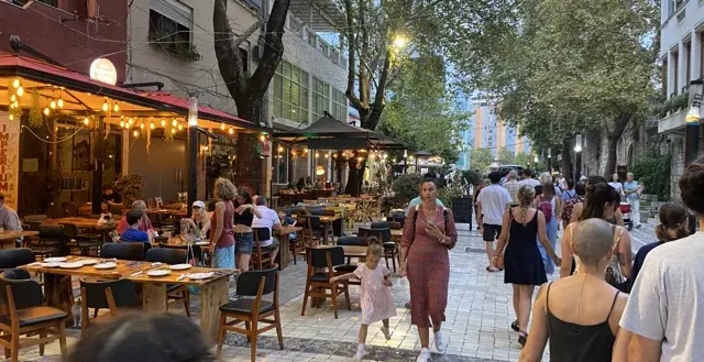 Bustling city street at night with outdoor restaurants and pedestrians.