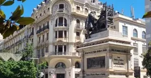 A beautiful fountain and ornate building in a sunny Spanish square.