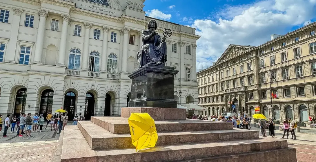 Bronze statue of Nicolaus Copernicus with an armillary sphere in Warsaw, in front of the Staszic Palace under a blue sky.