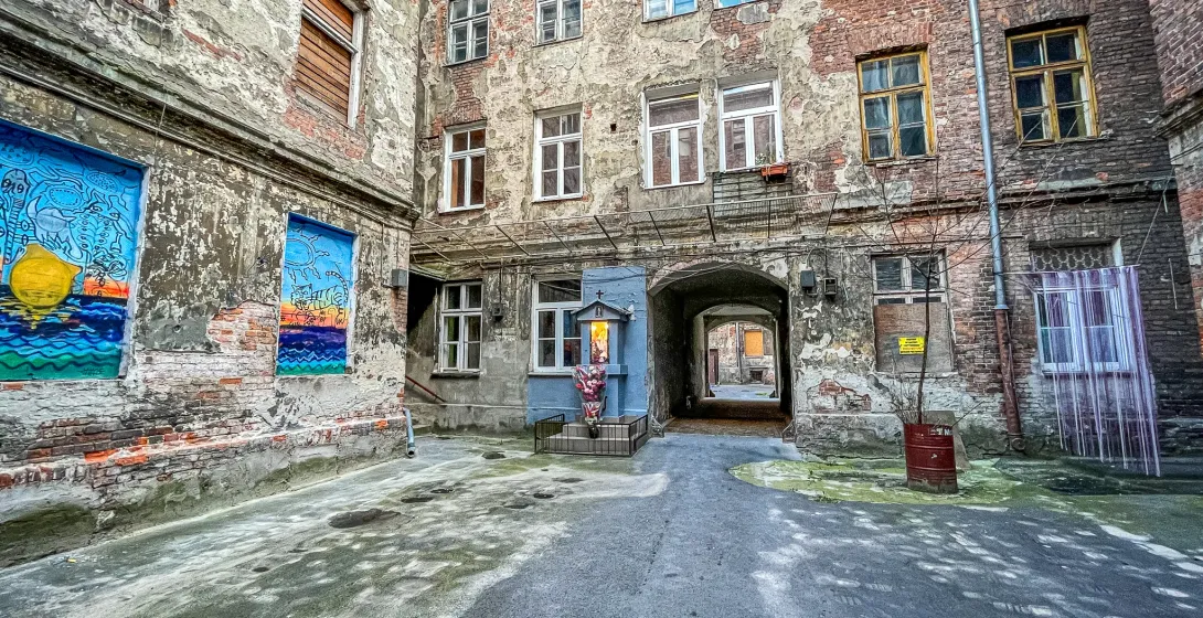 Explore a hidden Warsaw courtyard with aged brick buildings, street art, and a small shrine.