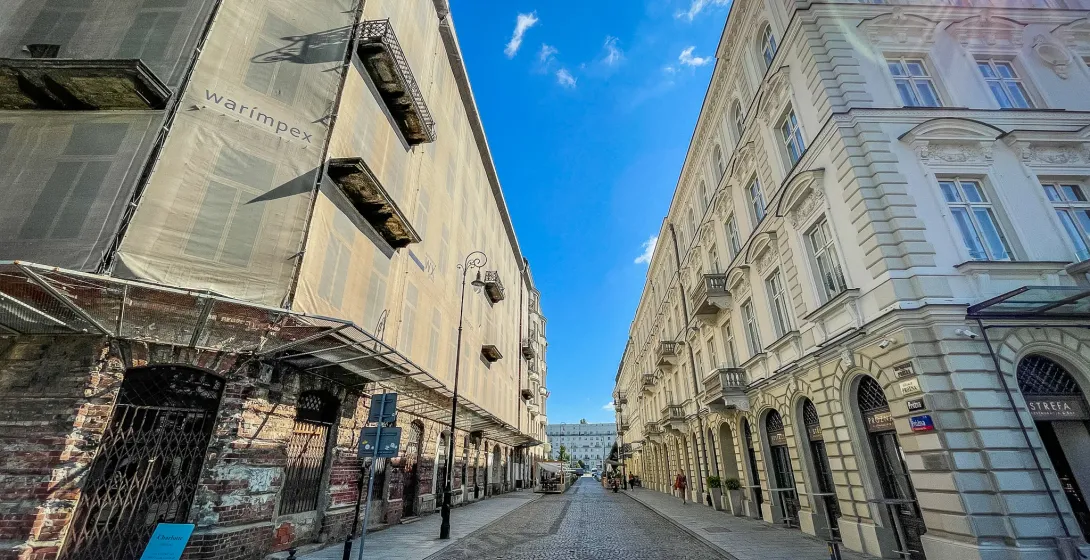 Sunlit cobblestone street in Warsaw, Poland, with historical buildings and one under renovation.