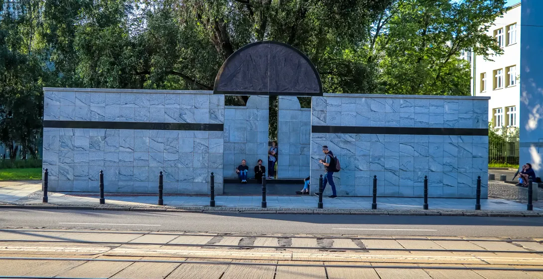 A modern marble memorial in Warsaw, Poland, with people nearby.