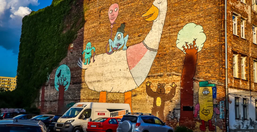 Colorful mural of a giant goose and other cartoon characters on a brick building in Warsaw.