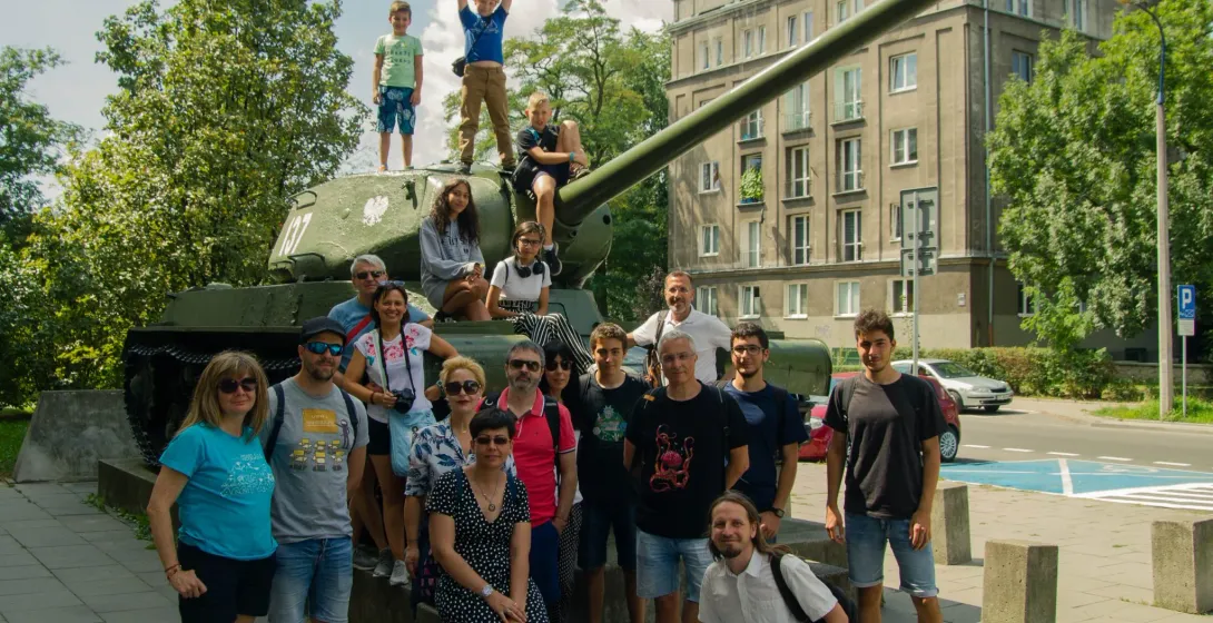 Happy tour group posing by a tank monument in Warsaw, Poland.