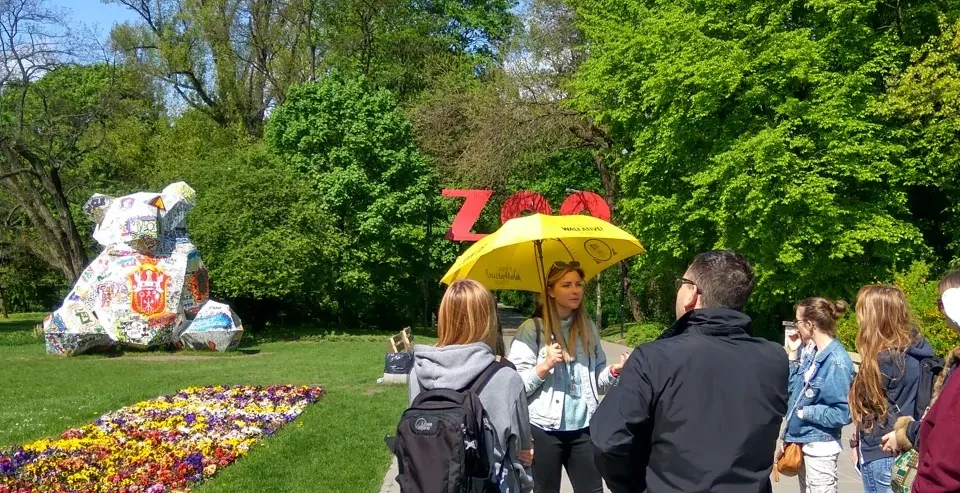 Guided tour group in Warsaw's park admiring a mosaic bear sculpture.