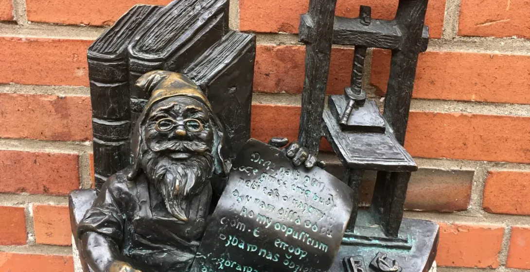 Bronze dwarf statue in Wrocław, Poland, sitting by a printing press and books.
