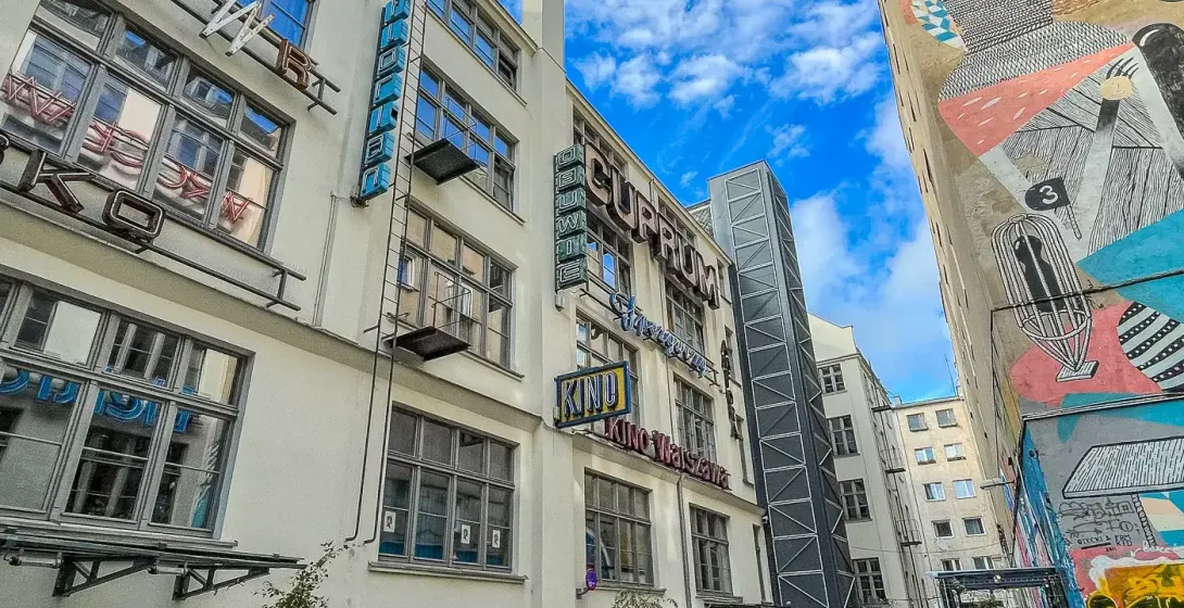 A narrow cobbled alleyway in Wrocław, flanked by a building with neon signs and another with a large abstract mural. Outdo...