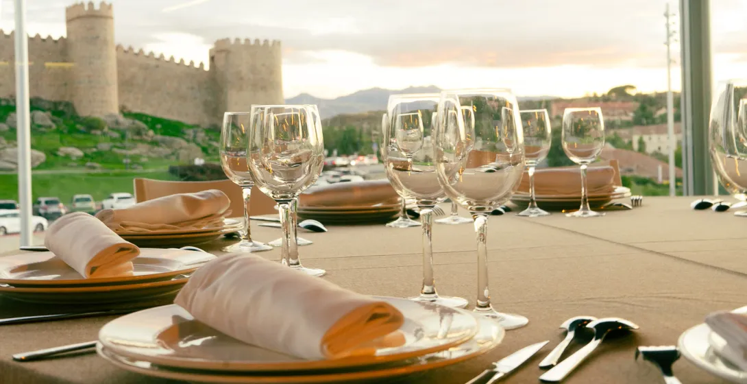 A dining table set with glasses and plates, overlooking the medieval city walls of Ávila, Spain at sunset.