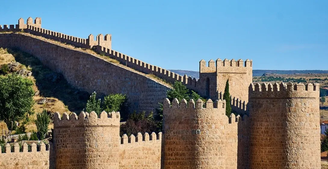 The medieval stone walls of Ávila, with their battlements and towers, on a sunny day with a clear blue sky.
