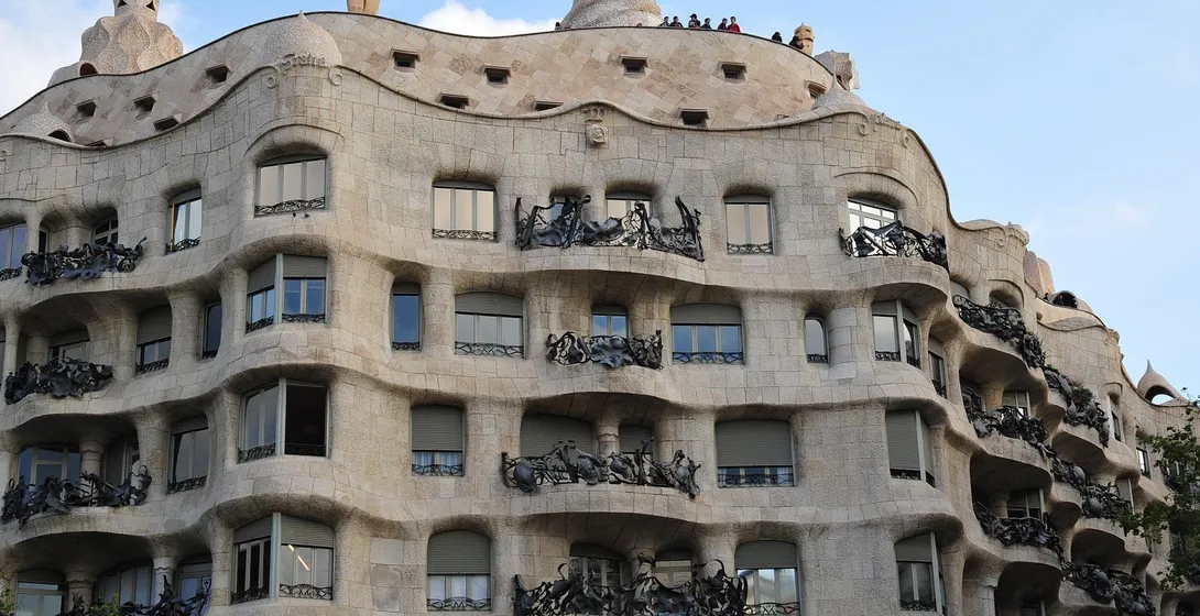 Curved stone facade of Casa Milà (La Pedrera) with ornate iron balconies under a blue sky, designed by Antoni Gaudí.