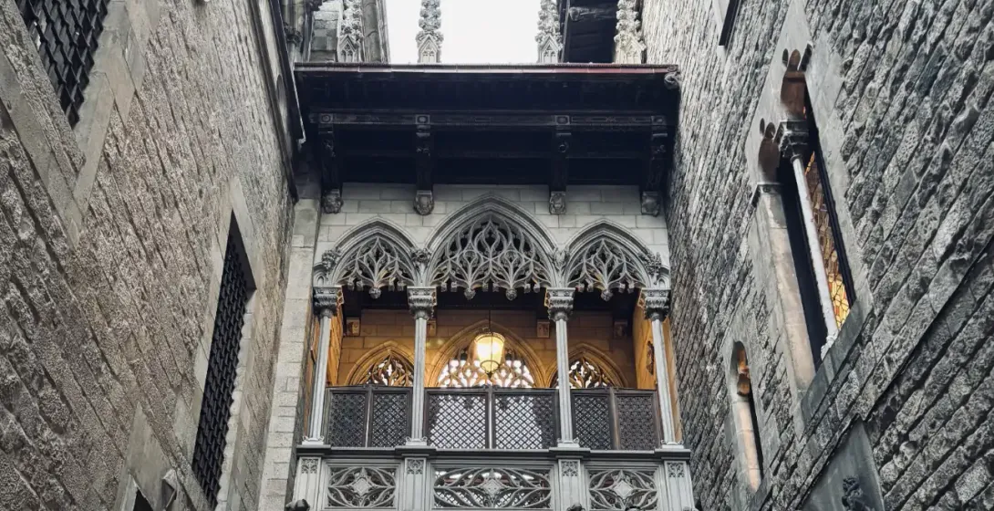 Ornate stone neo-Gothic bridge with a lantern and archway connecting two medieval-style buildings in a narrow alley.