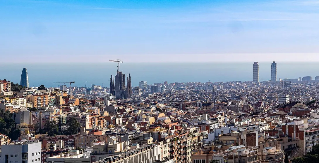 Panoramic view of Barcelona city with Sagrada Familia under construction, Agbar Tower, and two skyscrapers by the sea.