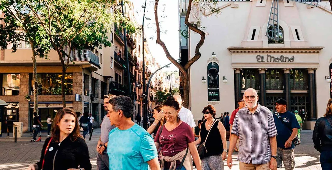 Group of people walking on a sunny street past El Molino theatre with a windmill on its facade in Barcelona.
