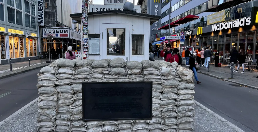 Reconstruction of Checkpoint Charlie guardhouse with sandbags and a plaque on a cobblestone street in Berlin, with buildin...