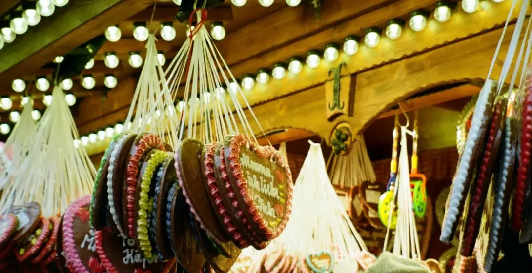 Hanging gingerbread heart cookies with icing decorations and various sweets at a festive market stall, with people browsing.