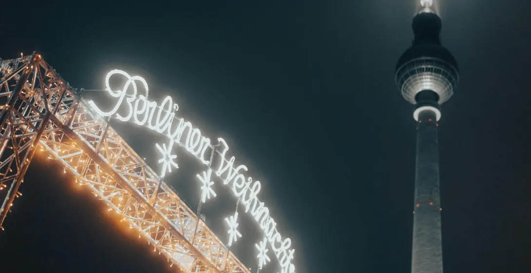 Illuminated 'Berliner Weihnachtszeit' sign and a section of the Berlin TV Tower against a dark night sky.
