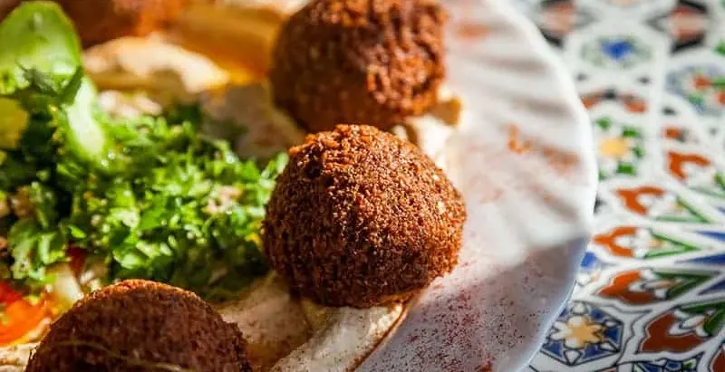 Close-up of a plate with several golden-brown falafel balls, a spread of hummus, and green chopped parsley salad.