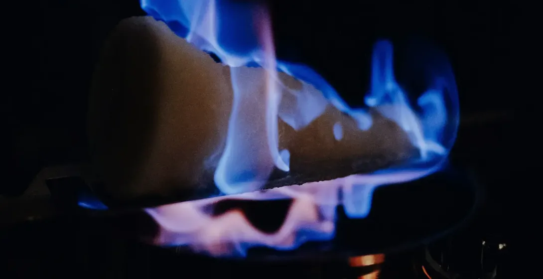 Sugar cone with blue flames burning over a dark pot, illuminating the foreground against a dark background.