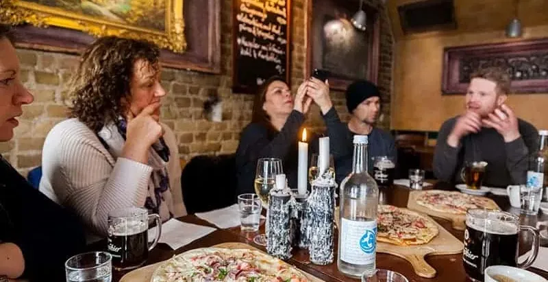 A group of people sitting at a long table in a cozy Berlin restaurant, with Flammkuchen and drinks in front of them.