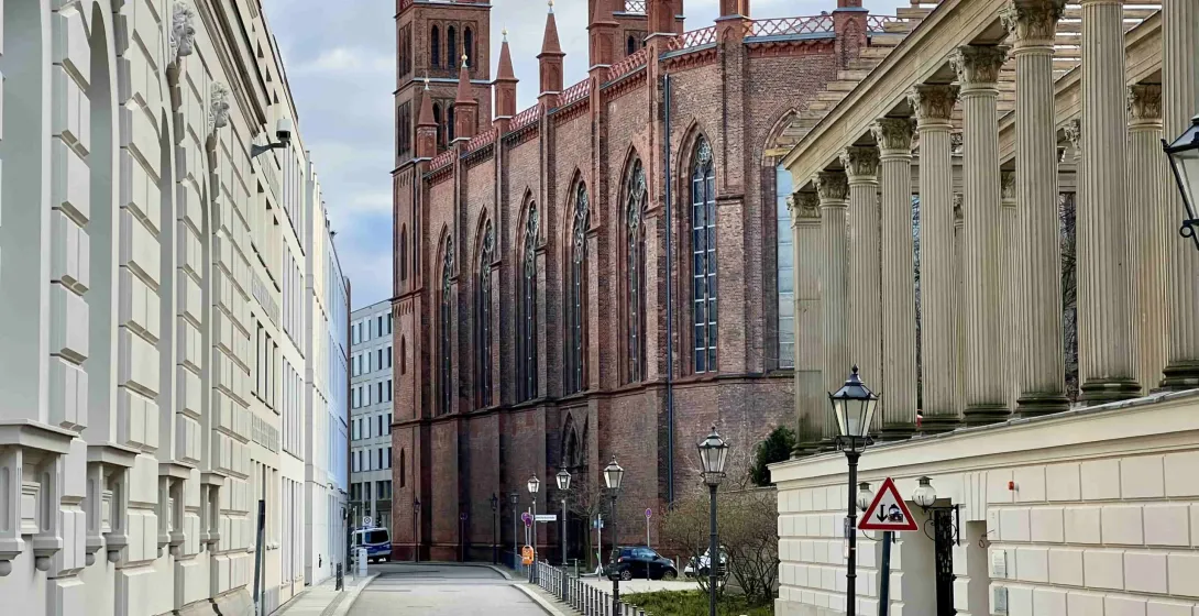 The red-brick Friedrichswerder Church seen from a quiet side street next to a building with a classical colonnade in Berlin.