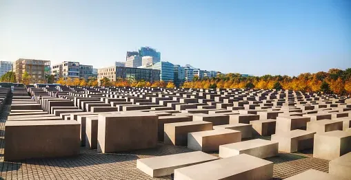 Concrete stelae of the Memorial to the Murdered Jews of Europe in Berlin on a sunny day with city buildings in the backgro...