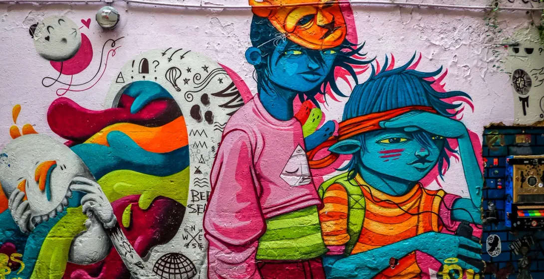 Colorful street art mural on a textured light pink wall depicting stylized blue-skinned figures and abstract elements.