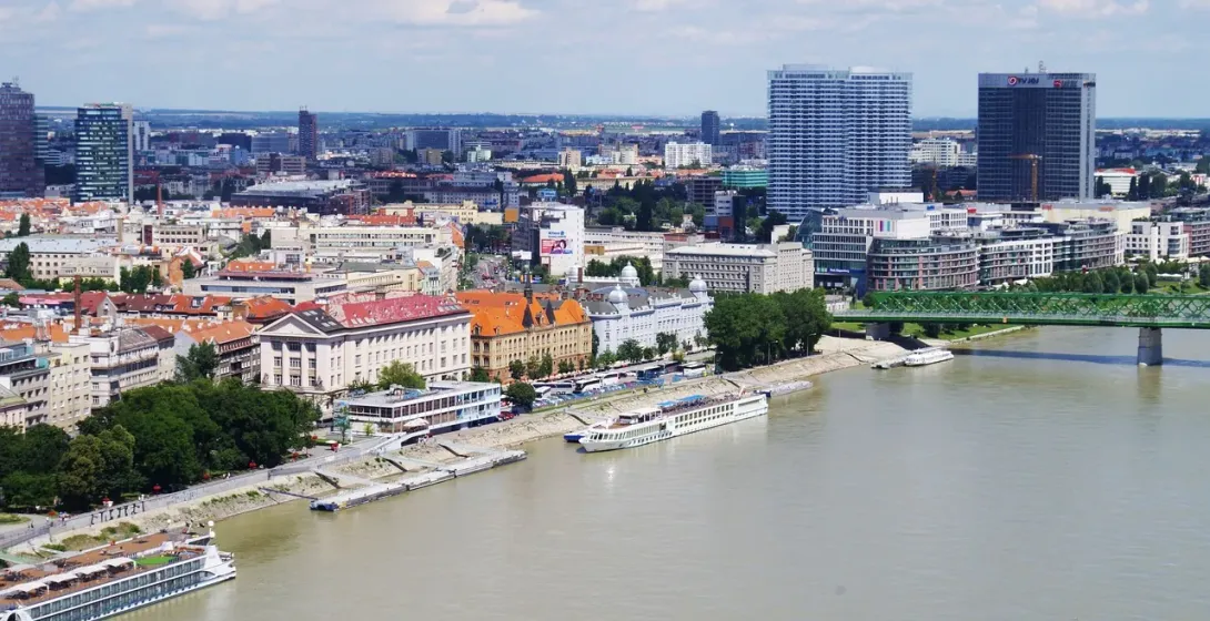 Aerial view of Bratislava cityscape along the Danube River, featuring modern skyscrapers, historic buildings, and a green ...