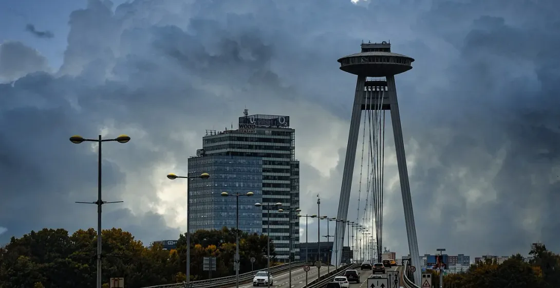 Modern UFO Bridge (Most SNP) in Bratislava with cars on the roadway, a distinctive saucer-shaped restaurant, under dramati...