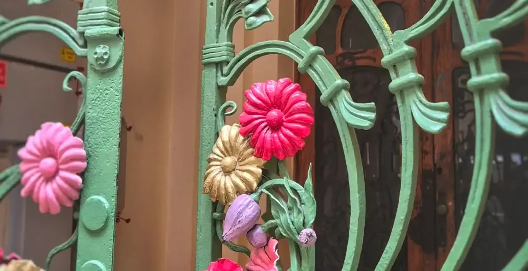 Ornate green Art Nouveau metal gate with colorful pink, gold, and purple floral decorations, in front of an arched wooden ...