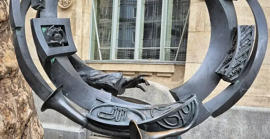 Bronze sculpture in Budapest featuring a man's head, hands, trumpets, piano keys, and abstract forms in a circular design.