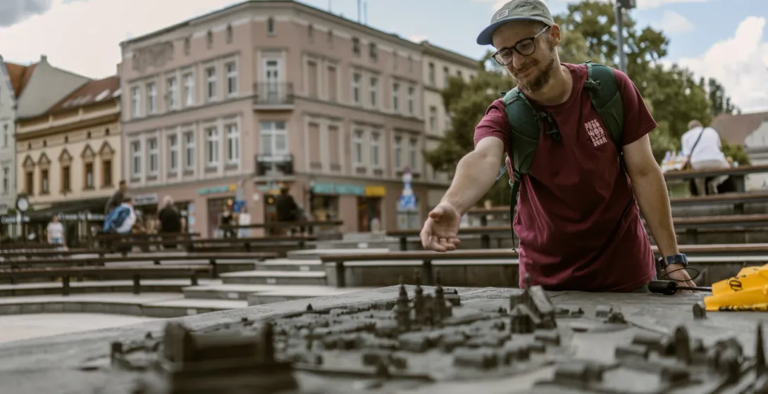 A man in a cap and glasses looks at a bronze model of the Old Town, with historic buildings in the background.