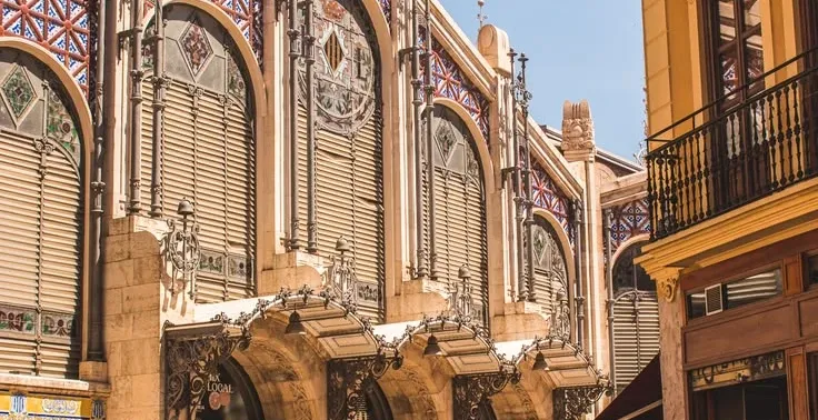 Ornate facade of the Central Market in Valencia, with people walking past on a sunny day.