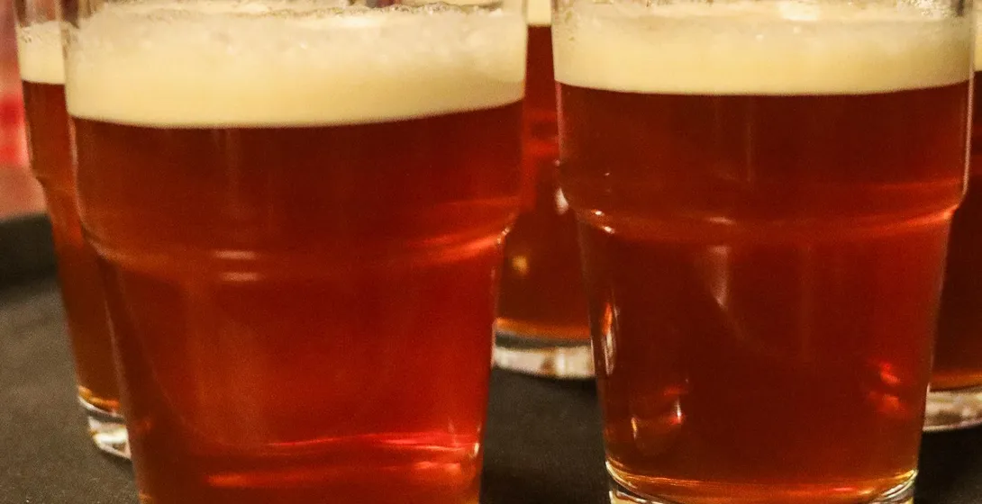 Several glasses of amber-colored beer with foam heads are arranged on a dark serving tray in a pub.