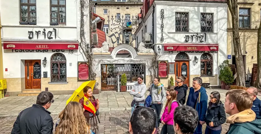 A tour group listens to a guide with a yellow umbrella on Szeroka Street in Krakow's Kazimierz district.