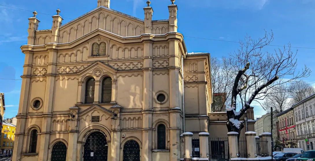Exterior view of a large, ornate synagogue with a Star of David, covered in snow, under a clear blue sky in Krakow.