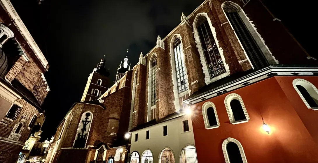 St. Mary's Basilica in Krakow at night, showing its brick facade, gothic windows, and two towers under a dark sky.