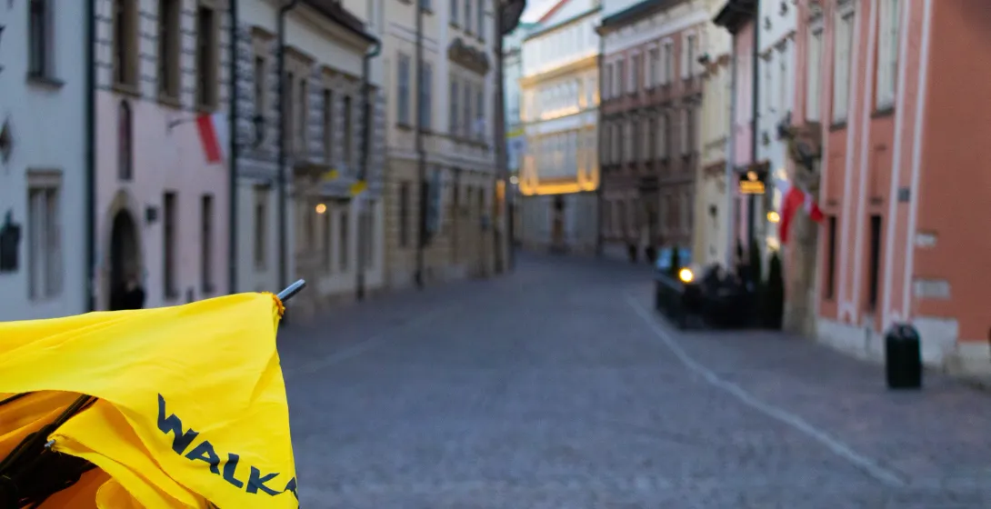 A yellow Walkative tour umbrella in the foreground, with a blurred view of a cobblestone street in Krakow's Old Town.