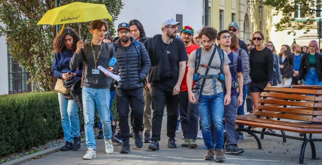A Walkative tour guide with a yellow umbrella leads a diverse group of tourists along a paved city street in Krakow.