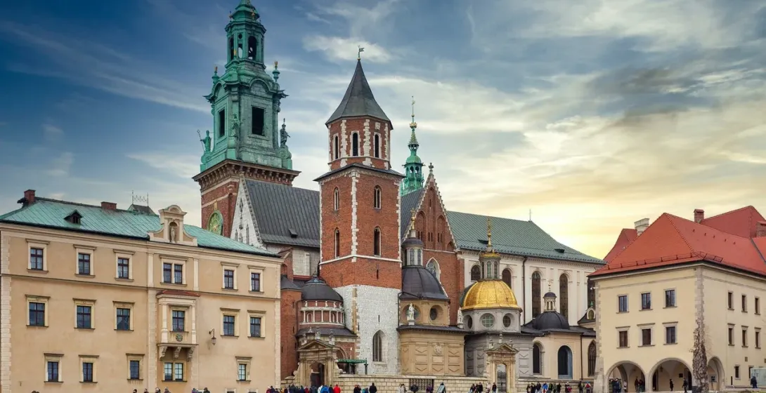 The Wawel Cathedral complex on a partly cloudy day, with its various towers and chapels seen from a grassy lawn.