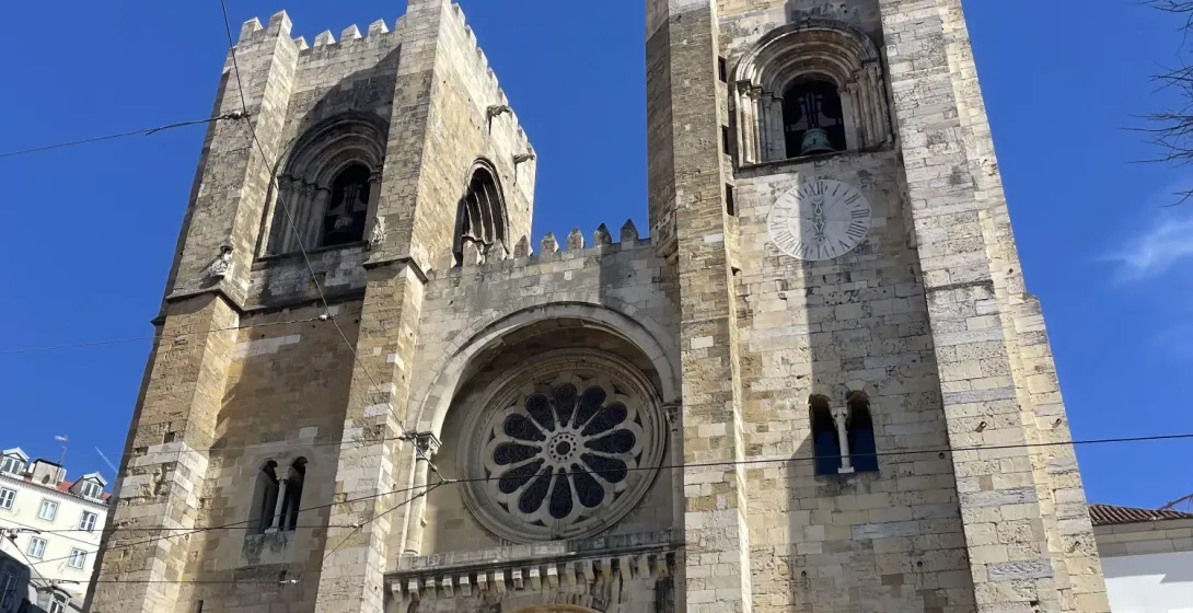 The facade of Lisbon Cathedral (Sé de Lisboa) with two square towers, a central rose window, and an arched entrance under ...