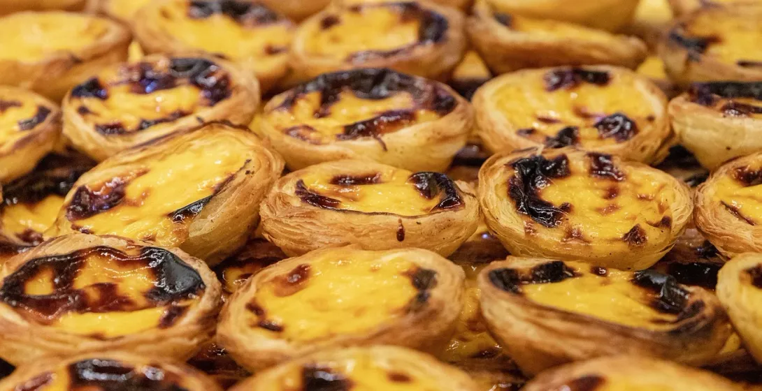A close-up view of many Pastéis de Nata, Portuguese custard tarts with a dark, caramelized top.