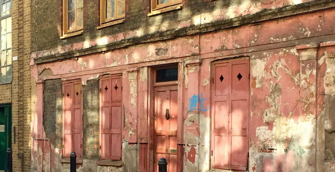 A 1700s weathered brick building with a faded pink ground-floor storefront, viewed from a street in London.