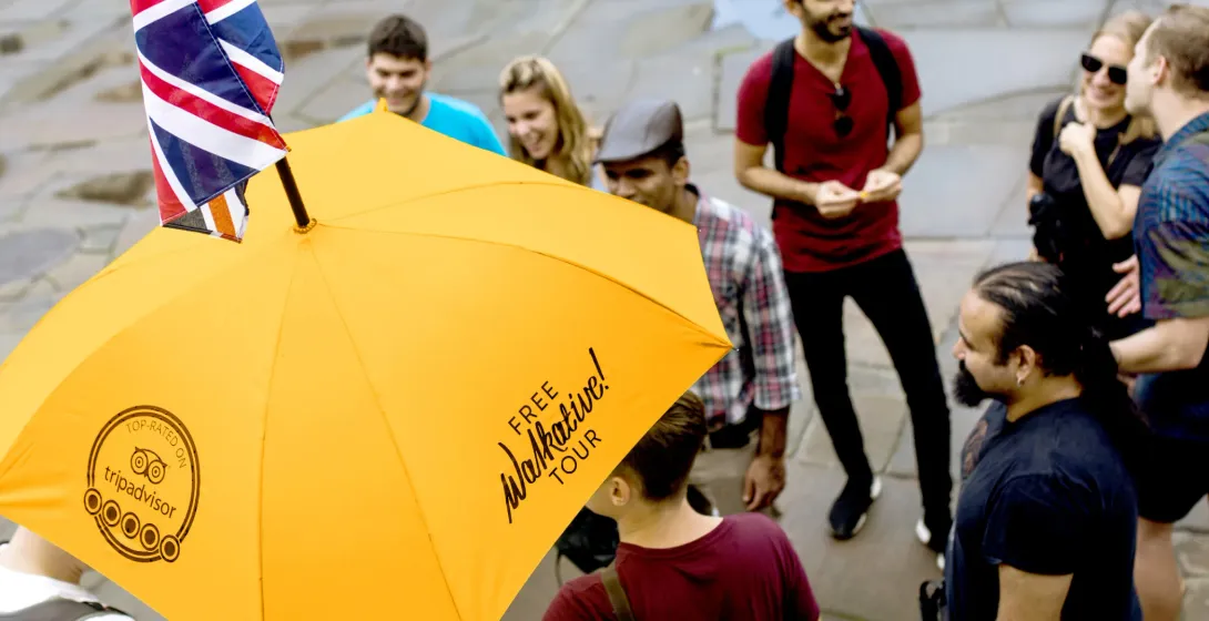A diverse group of people listening to a tour guide holding a yellow Walkative umbrella with a small Union Jack flag.